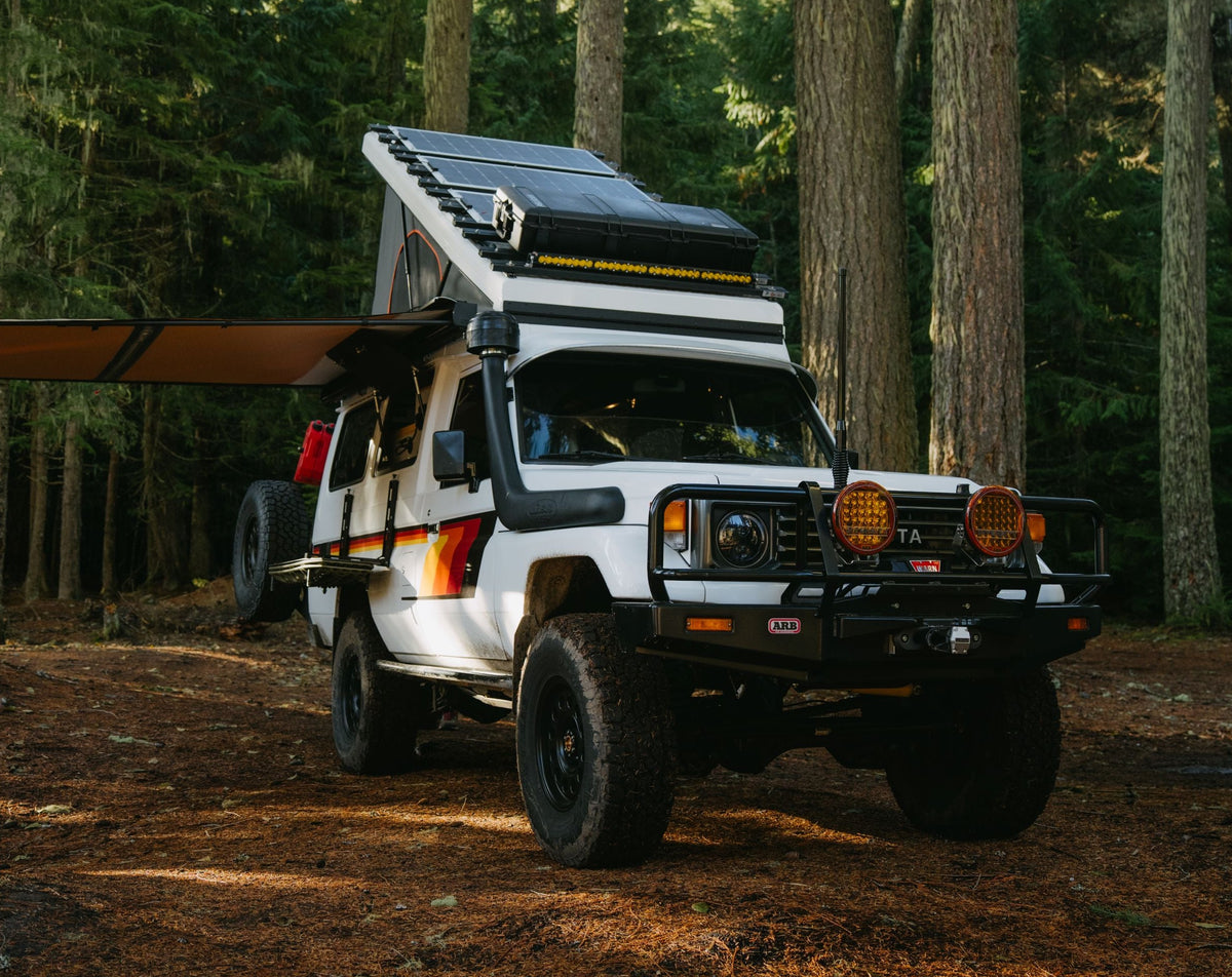 White Toyota Land Cruiser HZJ75 (Troopy) SUV with a pop top roof in a forest setting