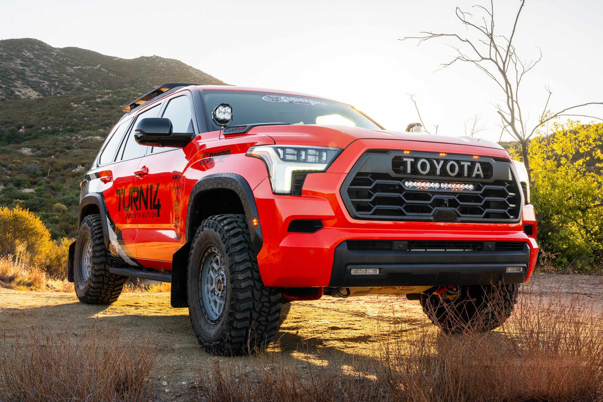 A red Toyota 4Runner TRD Offroad is parked on a dirt trail in a natural outdoor setting with hills and trees in the background.